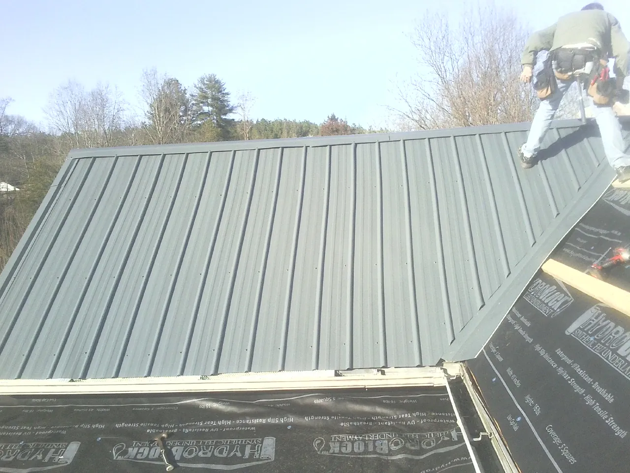 Crew installing dark green standing seam panels over synthetic underlayment in Whaleyville
