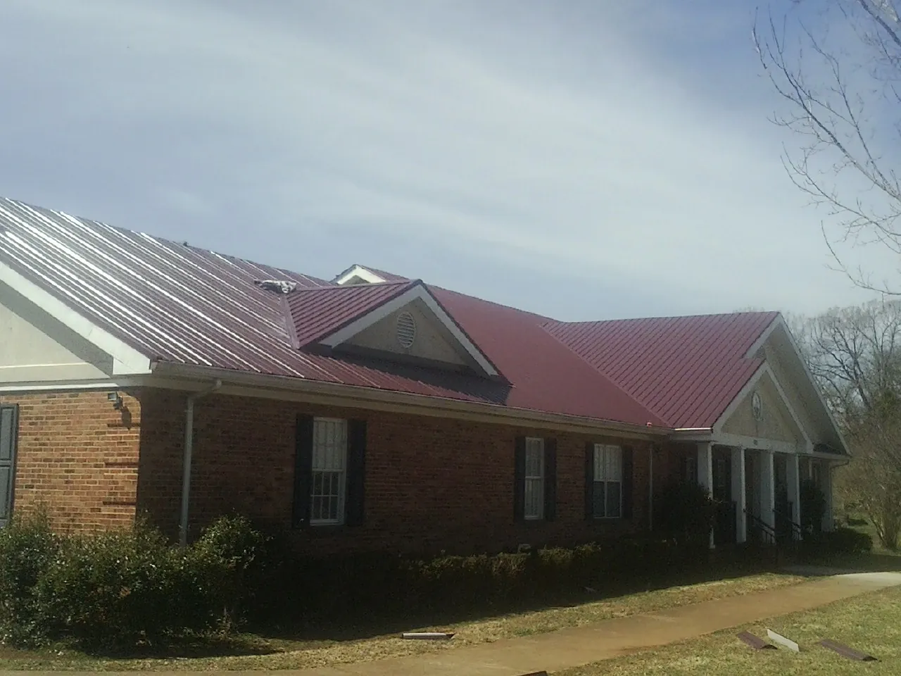 Red metal roof with gabled entries on a long brick building, from a Hail Damage Roof Repair job in Whaleyville