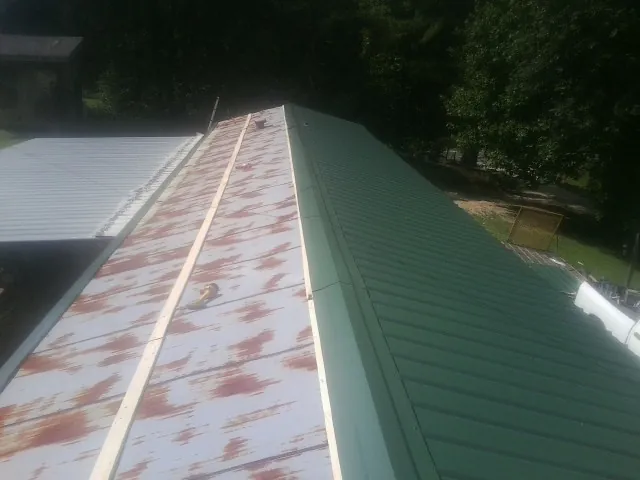 Old rusted panels beside newly installed green metal roofing — Wind Damage Roof Repair by Roofing Brothers in Whaleyville