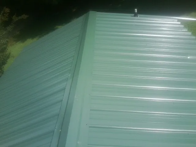 New green metal panels meeting at the ridge of a roof — Flat Roof Repair work by our crew in Whaleyville