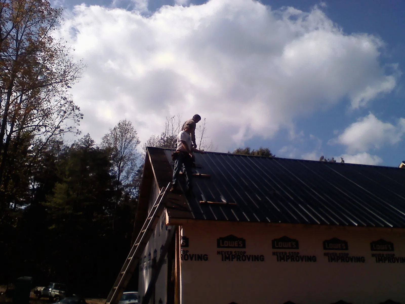 Roofer fastening dark metal panels high against a cloudy sky, from a Roof Inspection job in Whaleyville