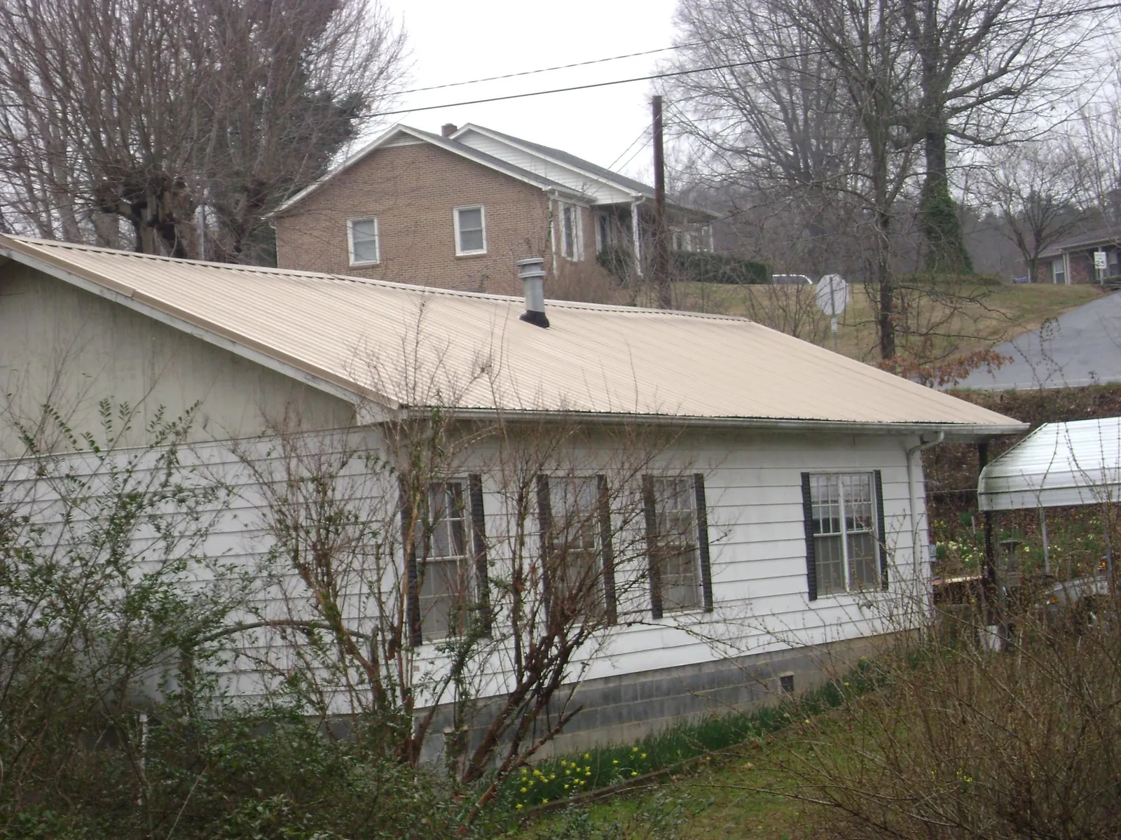 Tan metal roof on a white sided house set into a hillside — Commercial Roofing by Roofing Brothers in Whaleyville